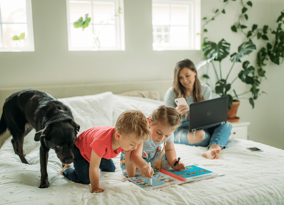 mom working on computer with kids and dog on the bed with her