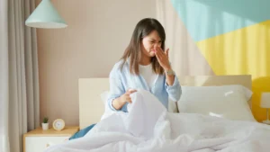 woman covering nose in bed with disgusted look on her face